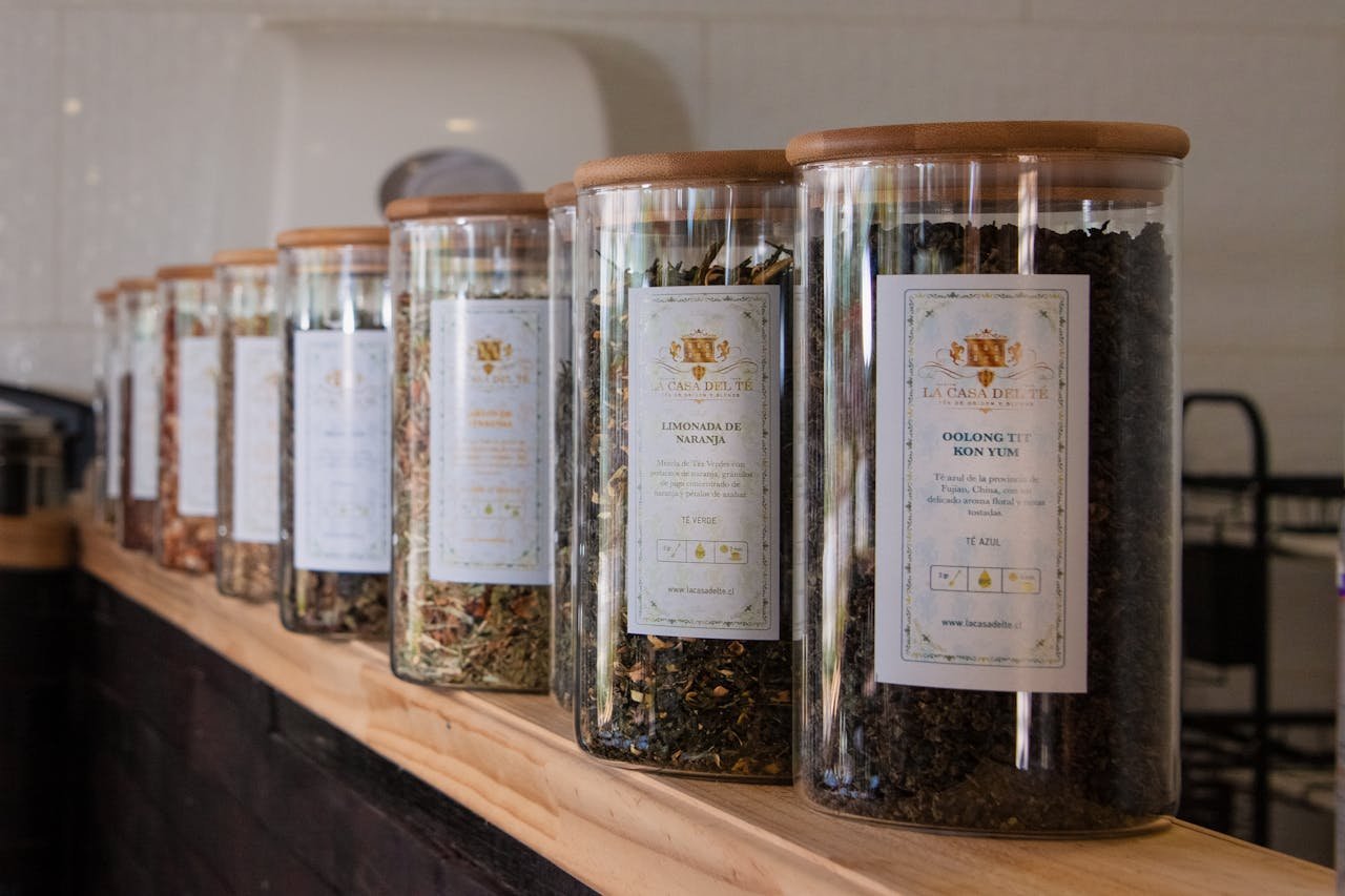 A selection of diverse loose leaf teas in labeled jars neatly arranged on a wooden shelf.